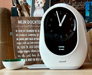 A medication dispensor clock standing on a table. 